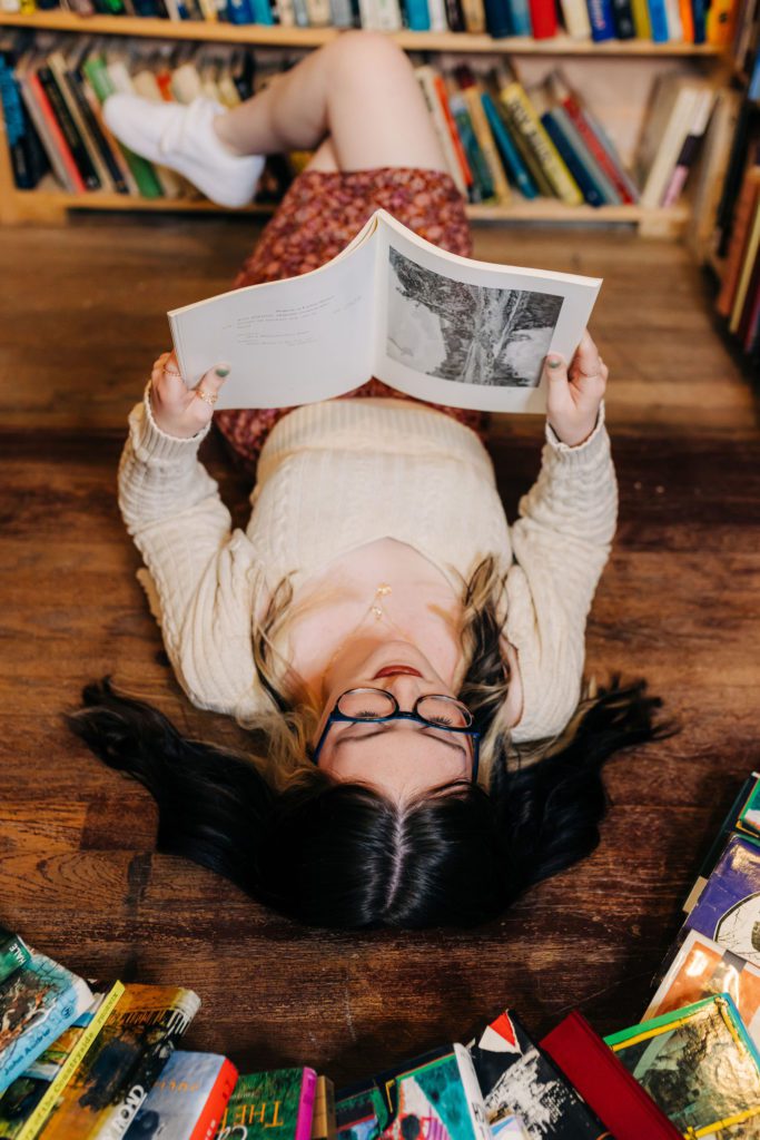 fun senior photo of senior girl lying on floor of local bookstore reading favorite novel