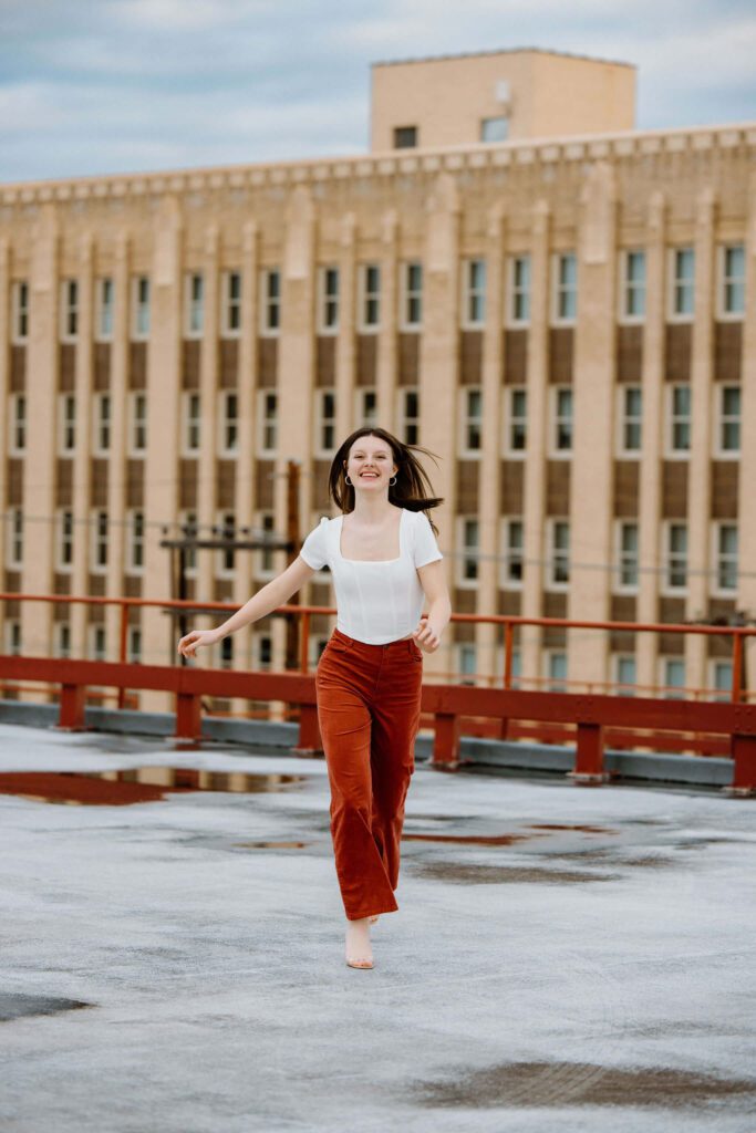 fun candid senior photo of graduate running on rooftop in white shirt and orange pants
