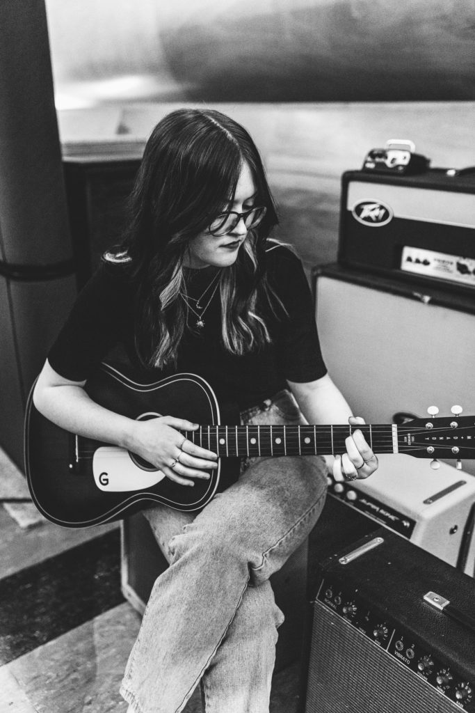black and white photograph of senior girl playing guitar while sitting in Mauldin Productions recording studio in Gladewater, TX