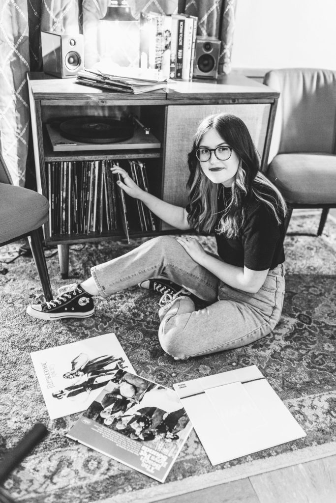 black and white photo of senior girl sitting on floor of Maulding Productions while looking through vintage records