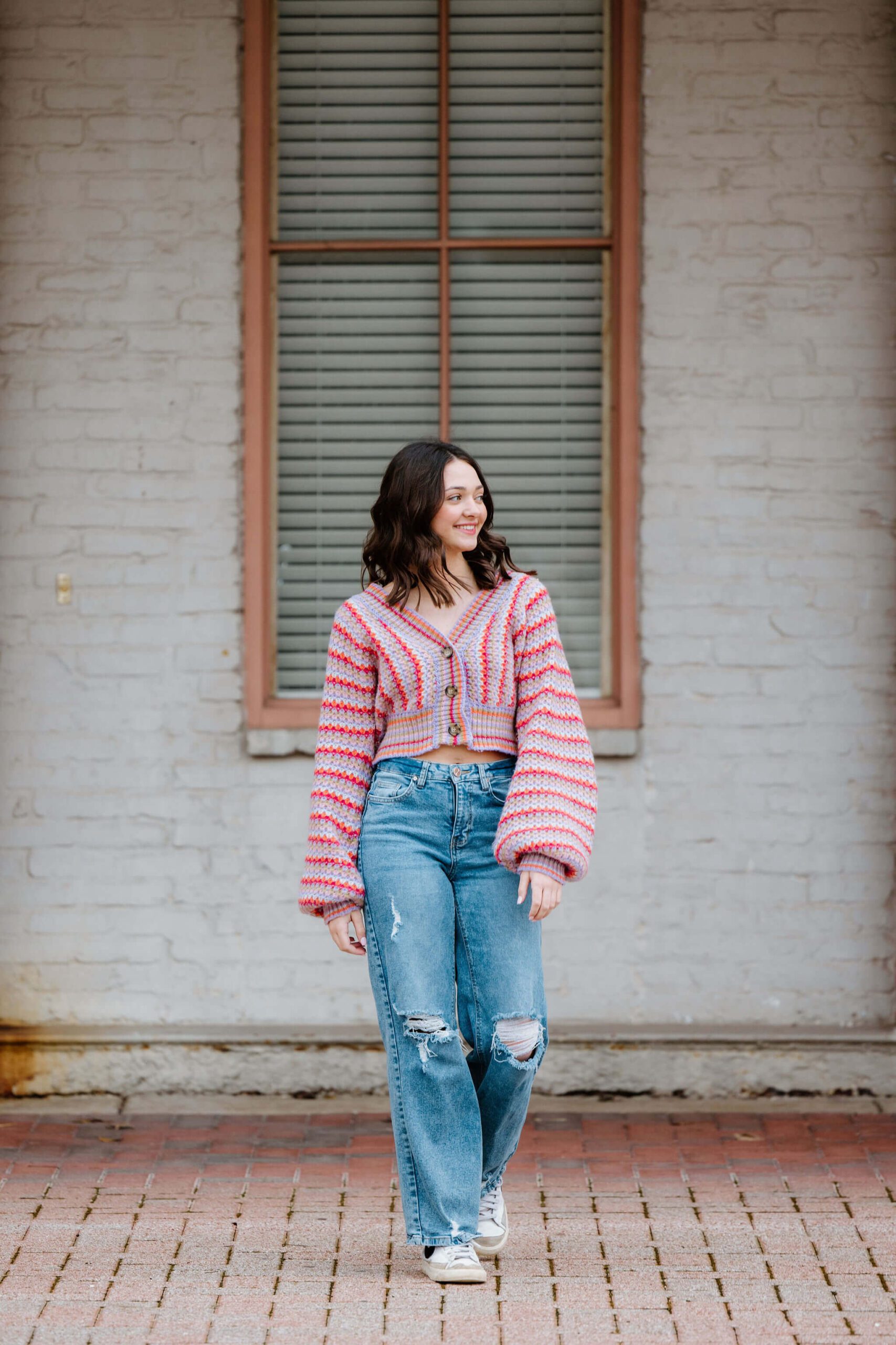 Candid senior photo of senior girl in stripped trendy sweater, denim jeans, and white sneakers walking in downtown Shreveport, LA