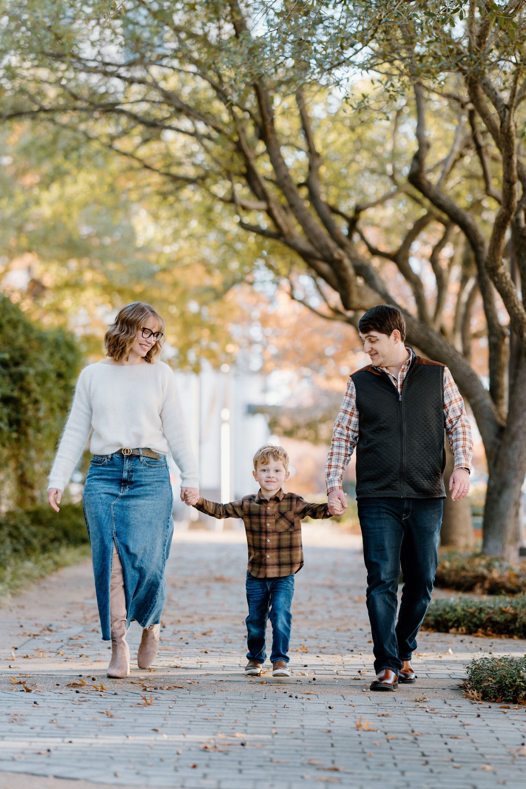 candid family photo of young family in neutral colors holding hands and walking on the sidewalk in downtown Longview, Texas