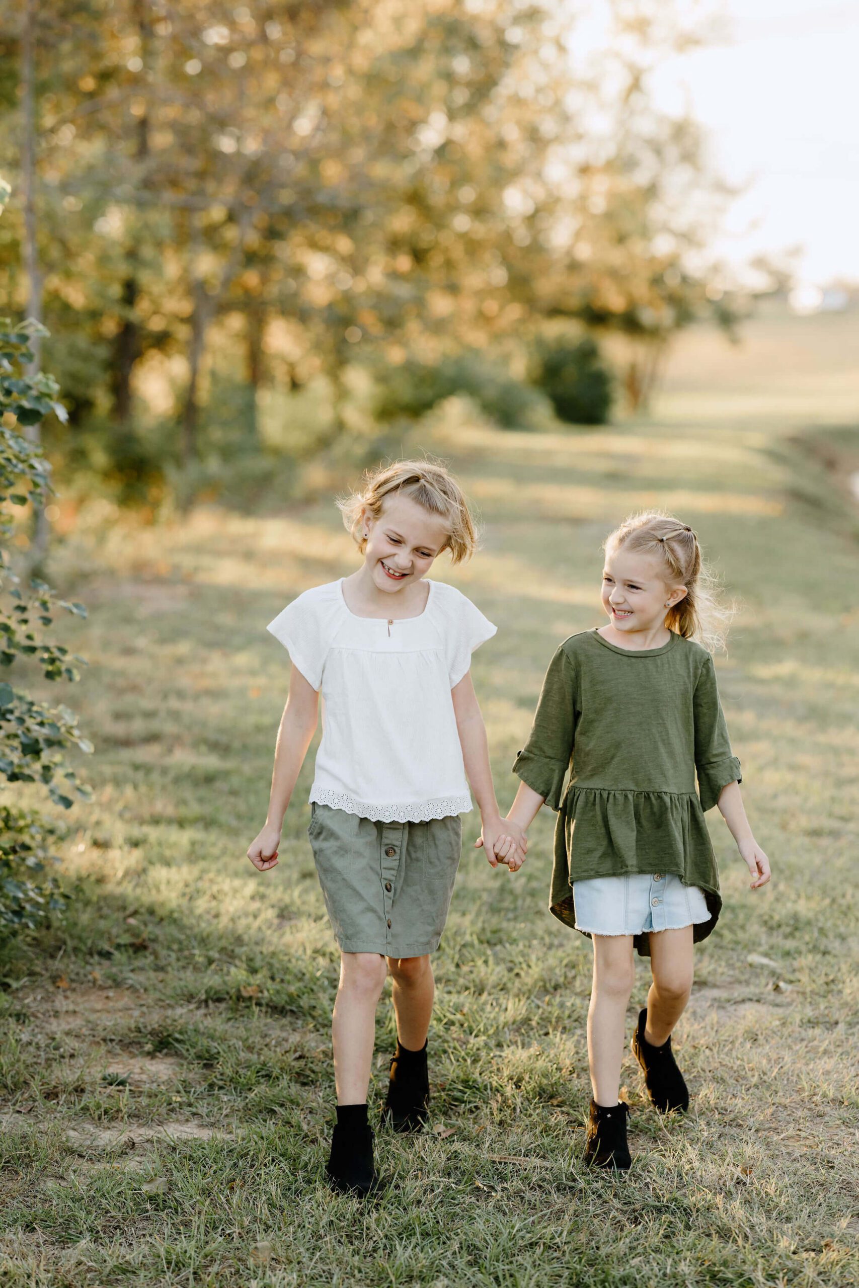 candid family picture of 2 young sisters holding hands and laughing as they walk through an open pasture