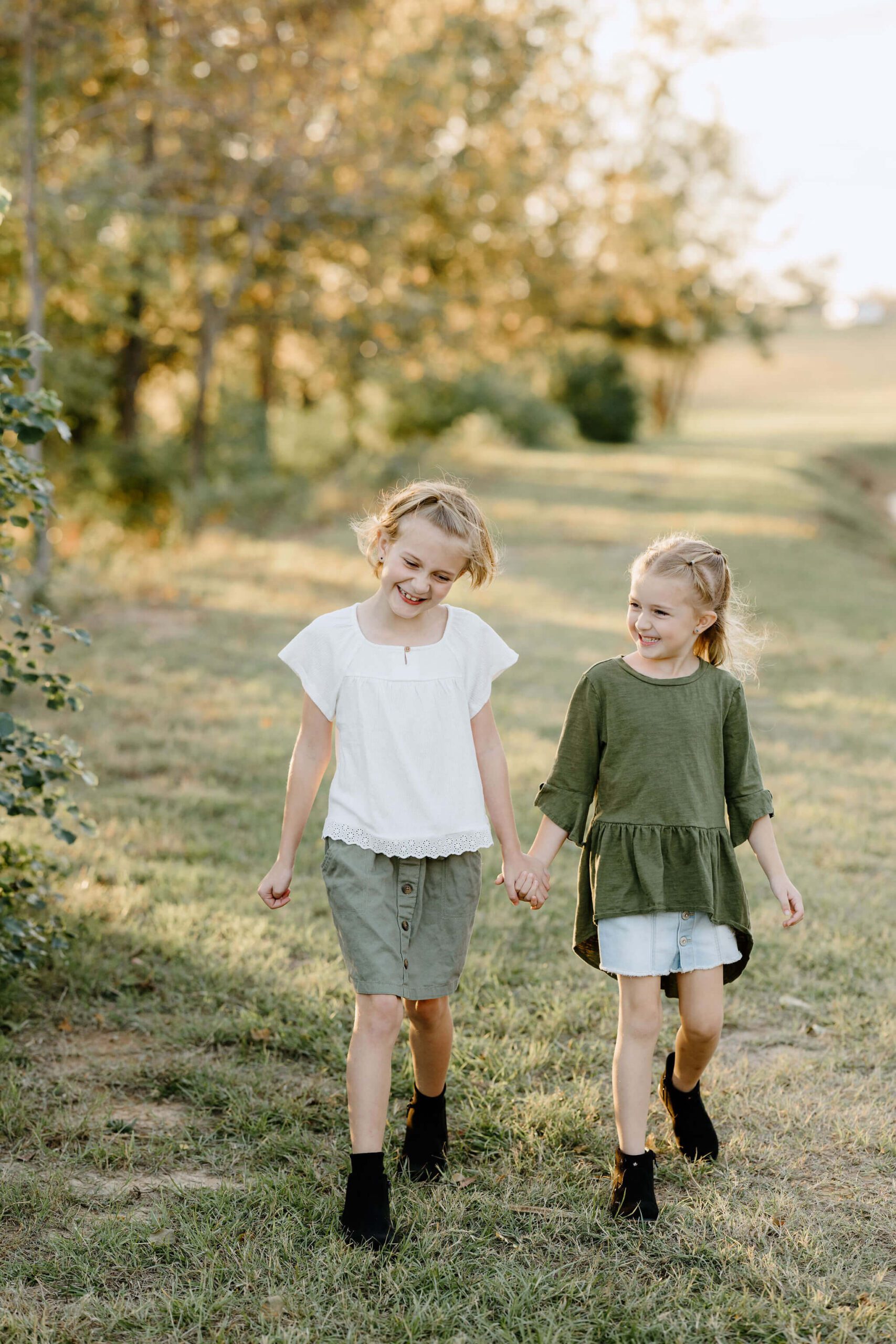 candid portrait of 2 sisters holding hands and laughing as they walk through field