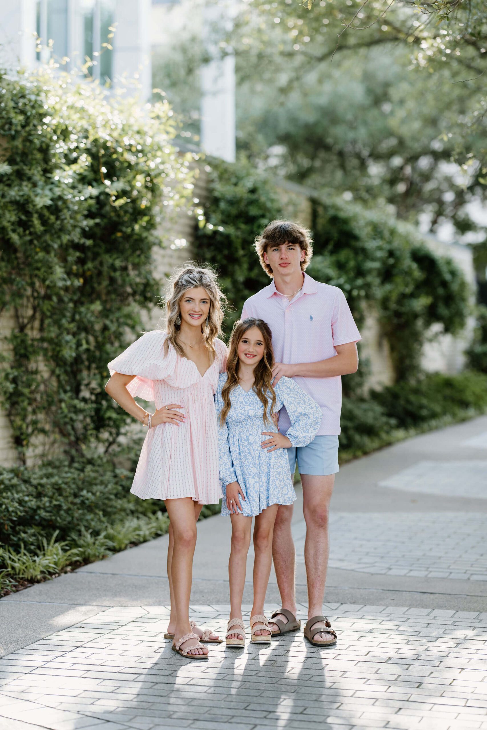 Family Portrait of siblings in coordinating blue, pink, and white outfits standing in front of wall of greenery in Longview, TX