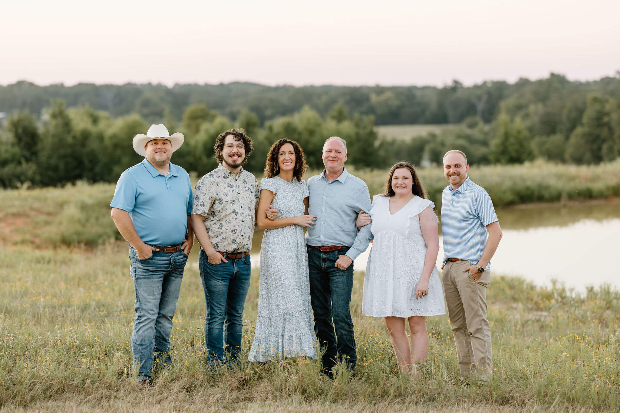 Family picture of family in coordinating summer wardrobe standing in open field at sunset
