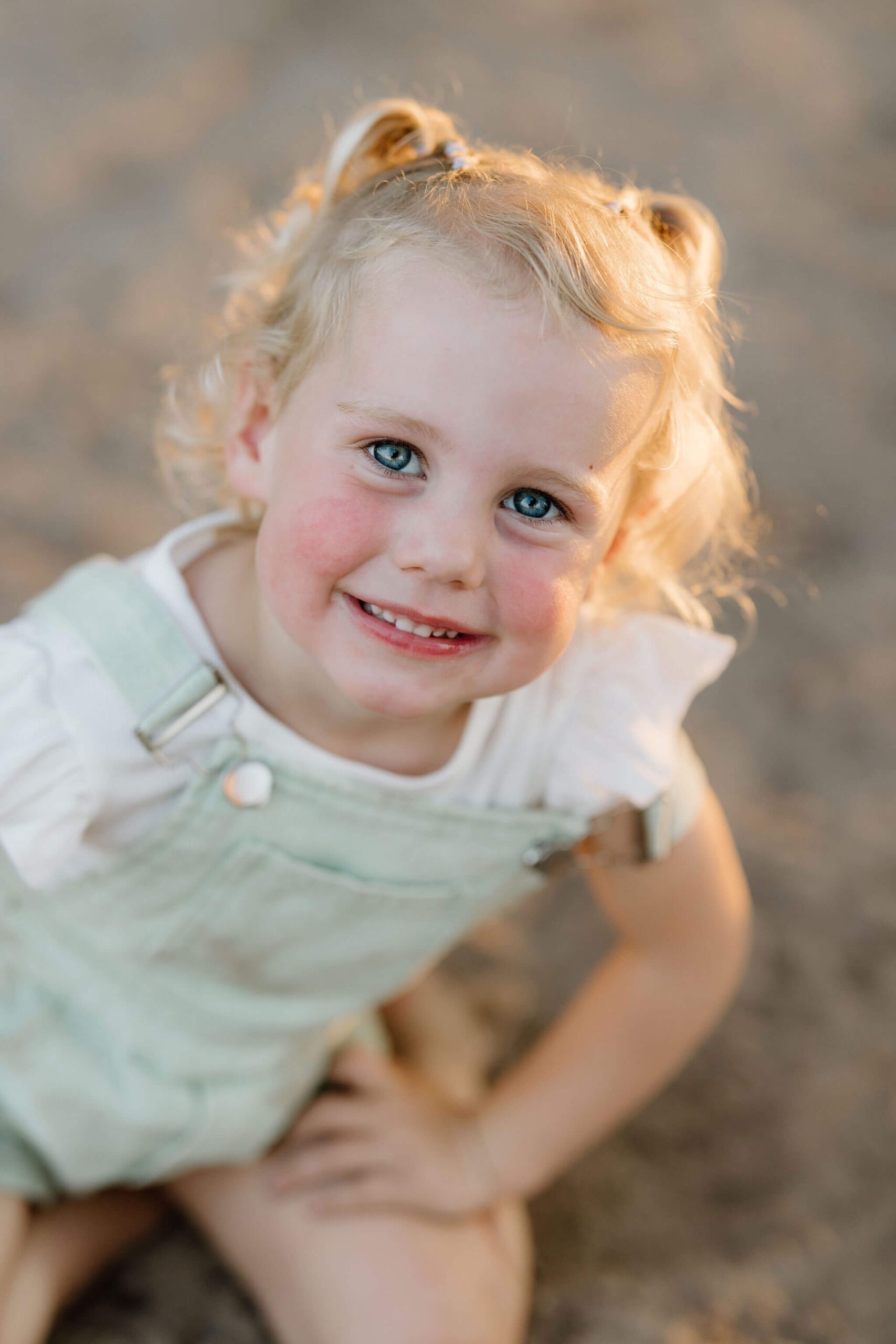 photo of 3 year old blonde girl in green overalls and white shirt smiling at camera