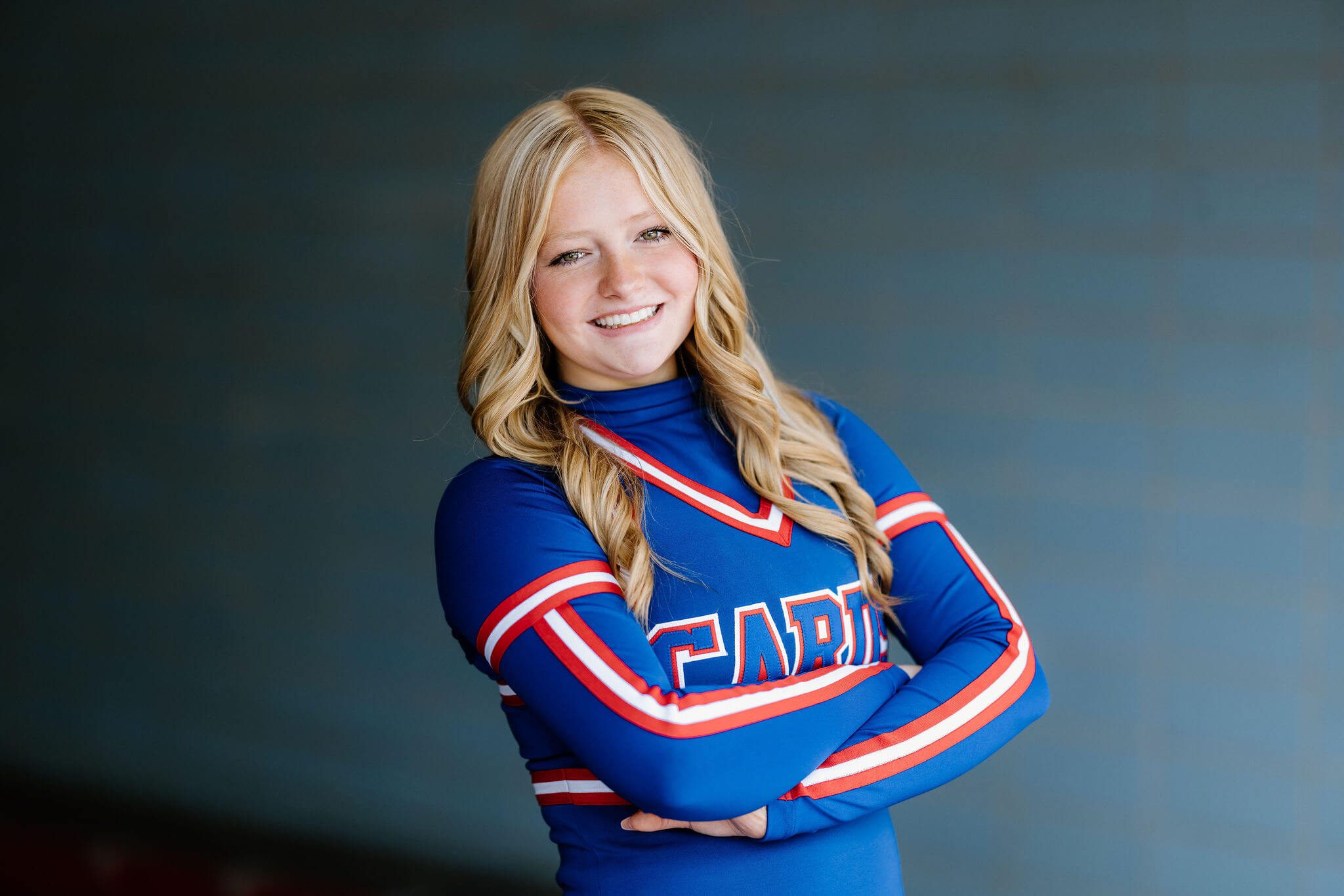senior girl in cheerleading uniform standing in front of blue background