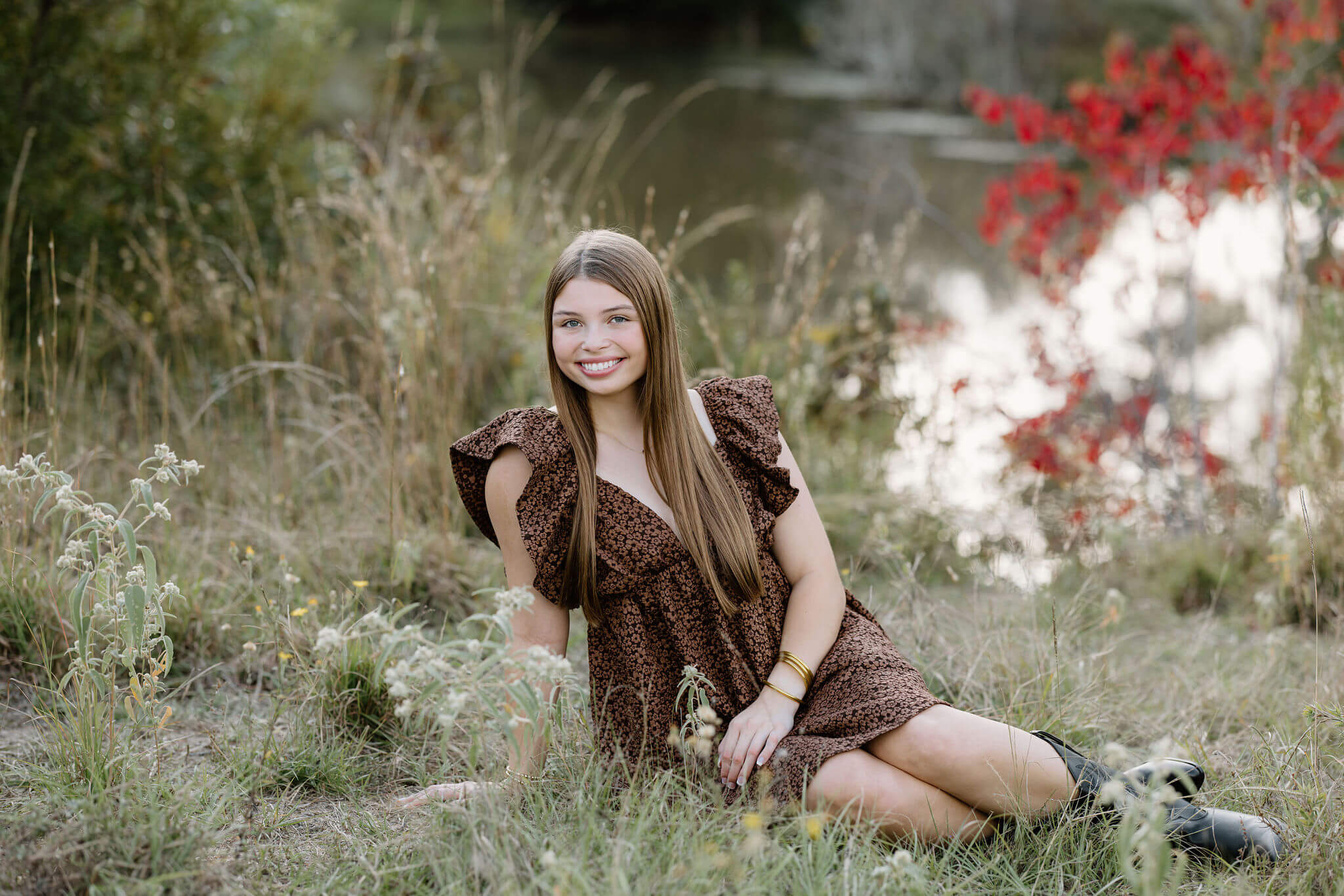 senior picture of graduate in brown dress sitting in field beside lake