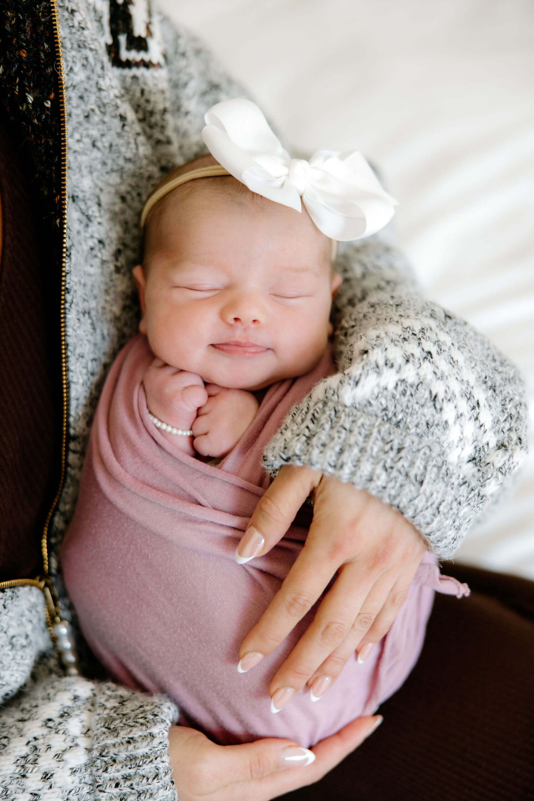 Newborn baby girl wrapped in a pink swaddle and held in her mother’s arms during an in-home lifestyle newborn photography session in Longview, Texas